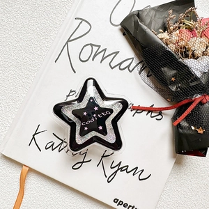 Star-shaped glitter phone grip with black and white sand flow effect on a book