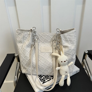 Quilted beige tote bag with silver chain straps and cute rabbit charm on black chair