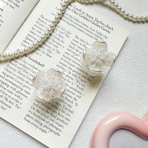 Close-up of white flower earrings with pearl texture on a vintage book and pearl necklace