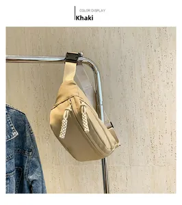 Detail of khaki nylon chest bag with white woven zipper pulls and black plastic buckle