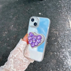 Close-up of a purple rhinestone heart phone grip on a reflective mirror case for iPhone