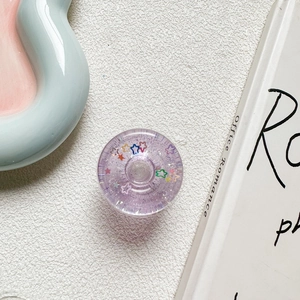 Macro shot of purple glitter star donut phone grip on white textured surface