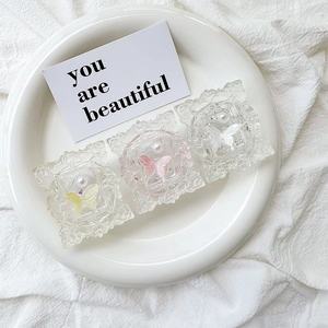 Detail of three aesthetic pastel butterfly resin charms with pearls on white fabric
