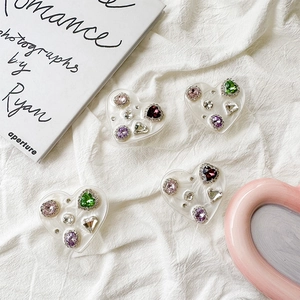 Detail of heart-shaped phone grips with colorful rhinestones on a white textured fabric