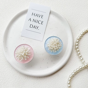 Pink and blue pearl flower phone socket grips on a white ceramic tray with soft lighting