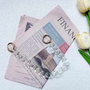 Close-up of iridescent acrylic bag chain strap with golden ring clasps on vintage paper