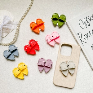 Cute shark slipper phone grip holders in various bright colors on a white textured background