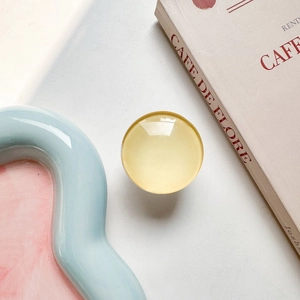 Close-up of a translucent yellow round phone grip stand on a soft pastel background