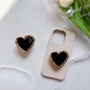 Detail of heart-shaped phone grip with gold textured edges on beige phone case