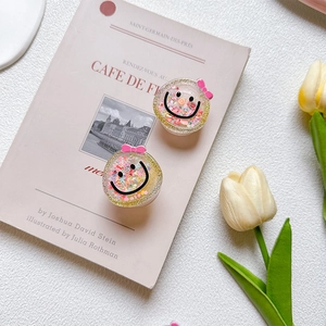 Close-up of glitter smiley face phone grips with pink bows on a soft pink background
