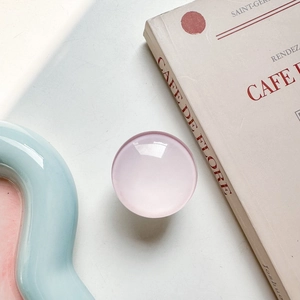 Detailed view of a pink translucent round phone grip on a vintage book and blue tray