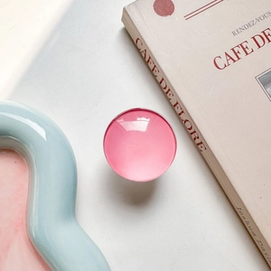 Close-up of pink glossy round retractable phone grip on a minimalist lifestyle setting