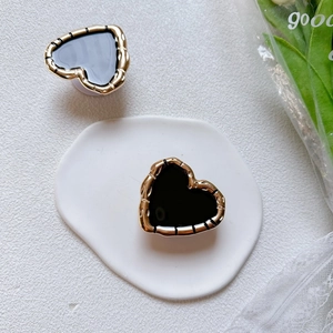 Detail of heart-shaped phone grip with gold wavy edge and black glossy center finish