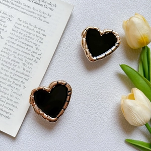 Macro detail of heart-shaped gold stud earrings with black enamel inlay on a magazine