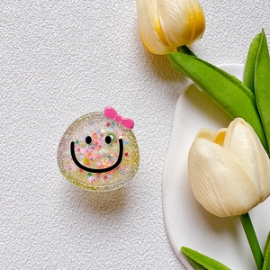 Glittery liquid phone grip with cute yellow smiley face and pink ribbon on white tray