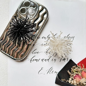 Silver wavy phone case with large radial bead charm accessory on fashion magazine