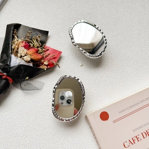 Close-up of oval silver folding mirrors with hammered metal texture on textured beige surface