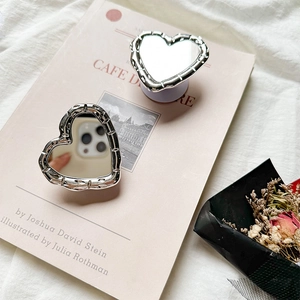 Close-up of heart-shaped mirror phone grip with silver wavy edges on a book