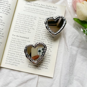 Close-up of heart-shaped mirror phone grip with silver bamboo texture on an open book