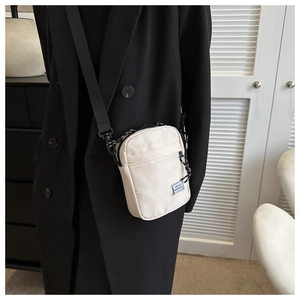 Close-up of a white mini nylon crossbody bag with black adjustable strap on a male model