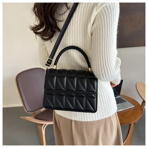 Modern black quilted handbag with woven handles worn by a model in a cafe setting