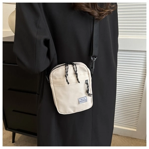 Detail showing cream crossbody bag with Hello Weekend label on black blazer jacket