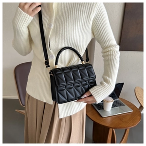 Chic black quilted shoulder bag with woven handle and gold hardware shown on a model