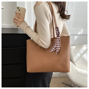 Close-up of caramel leather tote bag with vertical stitching and decorative checkered scarf