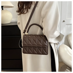 Detail of dark brown quilted leather handbag with woven handle and gold-tone hardware