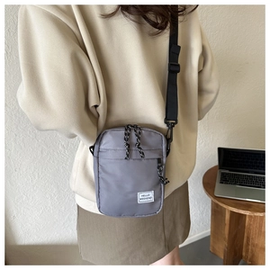 Close-up of grey oxford fabric crossbody bag featuring HELLO WEEKEND label on a wooden desk