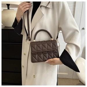 Detail of dark brown quilted bag with woven handle and gold hardware in a modern setting