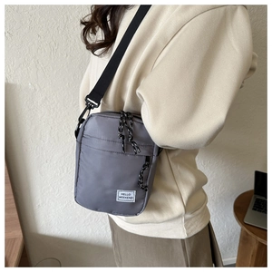 Close-up of grey nylon crossbody bag featuring Hello Weekend patch and woven zipper detail