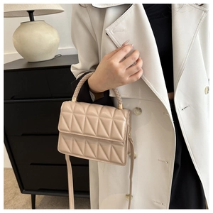 Detail of beige quilted handbag with woven handle and gold hardware on white coat
