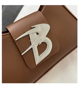 Dettaglio di una borsa baguette in pelle marrone con fibbia metallica a forma di uccello