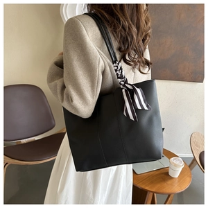 Detail shot of a black leather tote bag featuring a striped silk scarf handle decoration