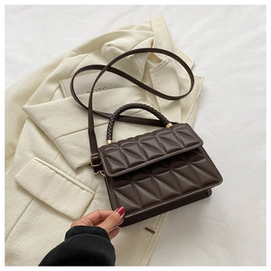Close-up of brown quilted handbag with woven handle on beige blazer background