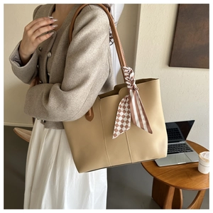 Detail of minimalist beige tote bag with checkerboard silk scarf handle on office desk