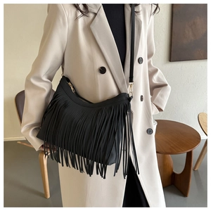 Close-up of a black fringe shoulder bag worn with a white blazer for a chic bohemian look