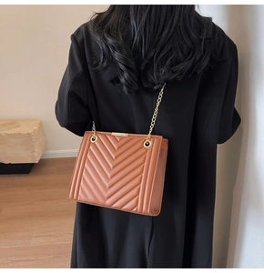 Close-up of brown quilted shoulder bag with golden chain strap and V-shaped stitching