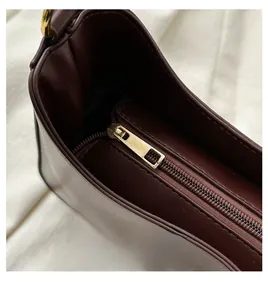Close-up of a smooth vintage gold metal zipper on a burgundy leather shoulder bag
