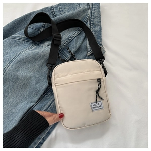Detail of beige nylon crossbody bag with HELLO WEEKEND patch on denim background