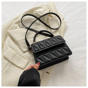Close-up of black quilted rhombus crossbody bag with braided handle on a suit backdrop