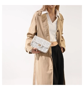 Détail d'un sac à bandoulière en tweed avec boucle dorée et chaîne élégante sur un trench