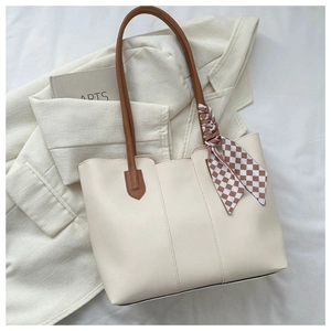 Detailed shot of cream tote bag with brown handles and a checked scarf accent