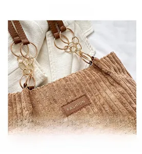 Detail of brown corduroy tote bag featuring a leather FASHION label and gold chain strap