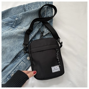 Detail of black mini crossbody bag with Hello Weekend patch on soft white fabric background