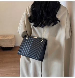 Detail of black quilted leather shoulder bag with gold chain strap on model in trench coat