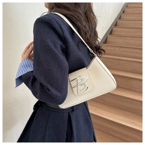Dettaglio di una borsa baguette beige con fibbia logo B argento portata come borsa da spalla