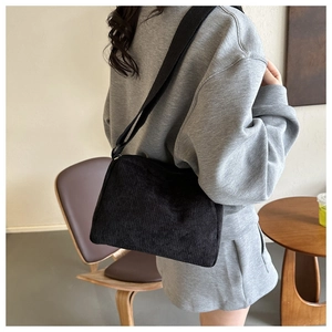 Minimalist black corduroy tote bag shown on a model in a modern interior setting