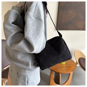 Detail of black corduroy shoulder bag showing vertical texture and adjustable strap on model